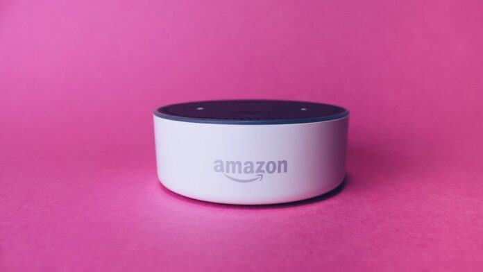 Criança sorridente fala próxima a um dispositivo de assistente virtual inteligente posicionado sobre uma mesa.