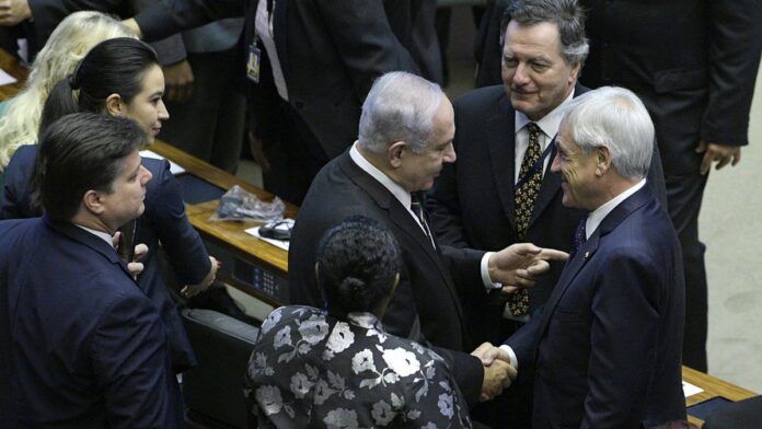 Rastros de luz de mísseis cruzando o céu noturno acima de uma cidade iluminada, com focos de incêndio ao longe.