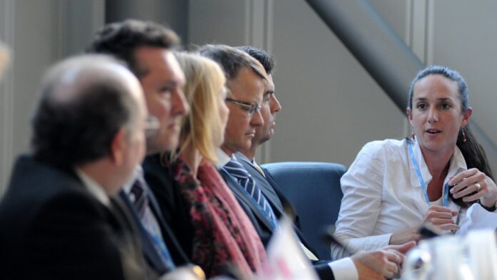 Mãos segurando um smartphone com o aplicativo do C6 Bank aberto, sobre uma mesa ao lado de papéis com documentos.