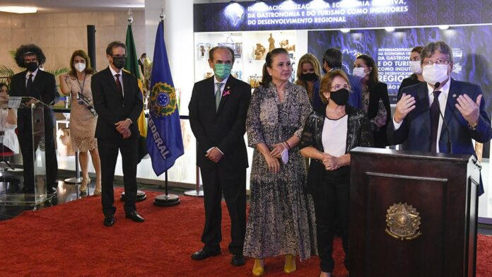 Ana Maria Lins entrega cadeiras de rodas a idosos em um evento na Paraíba, sorrindo durante a interação.