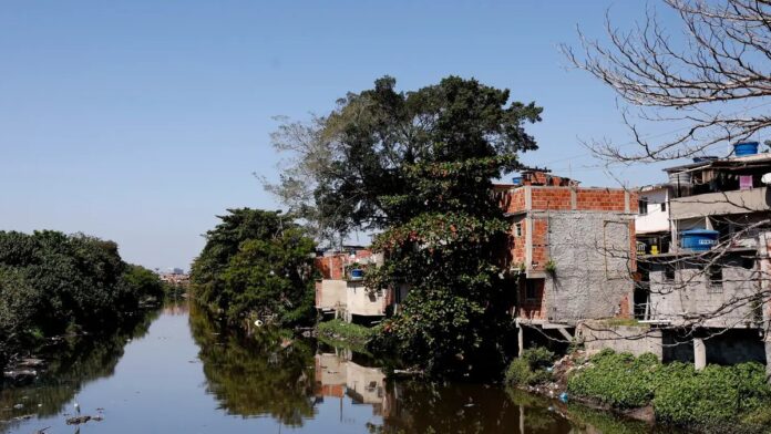 Moradores observam termômetro instalado em viela estreita de uma favela no Rio de Janeiro sob forte luz solar.