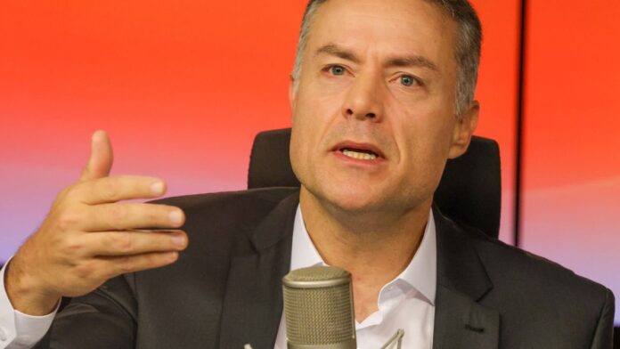 Caminhoneiro dirige caminhão em rodovia sob luz do dia, com foco na cabine e na estrada à frente.