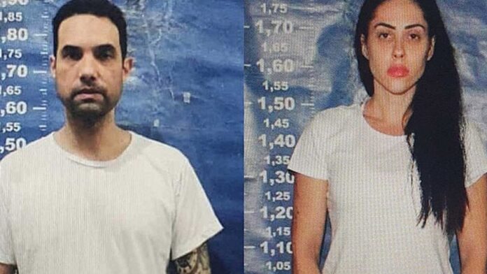 Jairinho e Monique sentados em um tribunal, com advogados ao redor e fotógrafos registrando o início do julgamento.