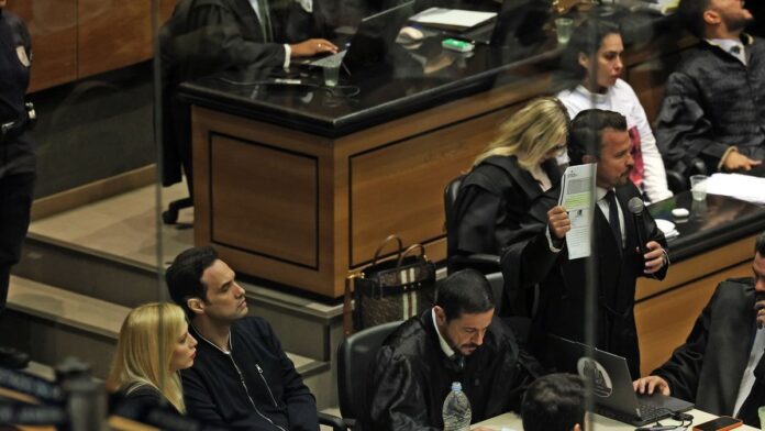 Monique Medeiros e Dr. Jairinho sentados lado a lado em uma sala de tribunal durante audiência judicial.