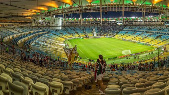 Jogador de futebol Cauan Baptistella, com uniforme azul do Cruzeiro, posa em campo durante partida.