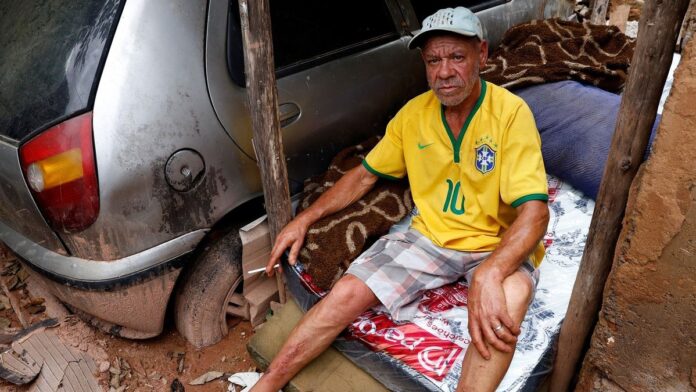 Morador caminha em rua com lama e escombros acumulados após enchente em Juiz de Fora.