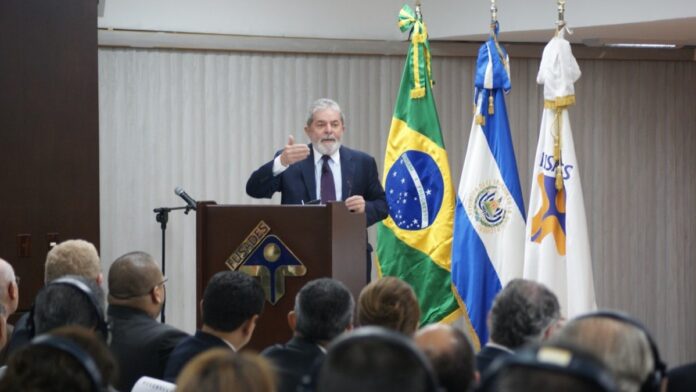 Bomba de combustível em posto com preços em destaque e reflexos de tráfego urbano ao fundo.