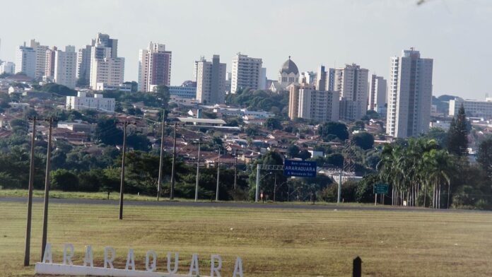 Operários com capacetes e coletes de segurança trabalham na estrutura de um prédio em construção em Araraquara.
