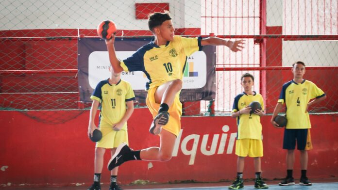 Jogadores de handebol de praia em disputa de bola na areia durante partida sob sol forte.