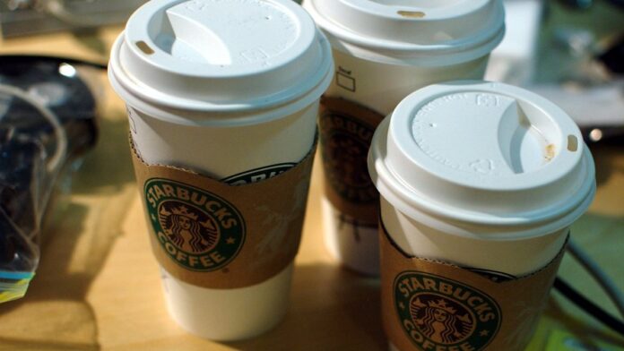 Pilha de copos de papel da marca Starbucks descartados incorretamente em uma lixeira de resíduos comuns.