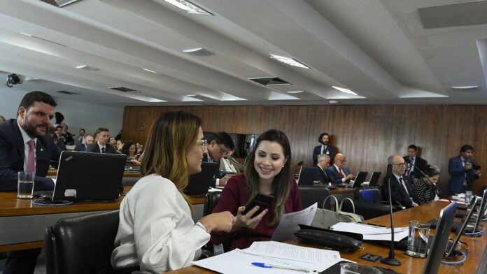Parlamentares em sessão no Congresso Nacional, sentados em bancadas, discutindo documentos durante votação.
