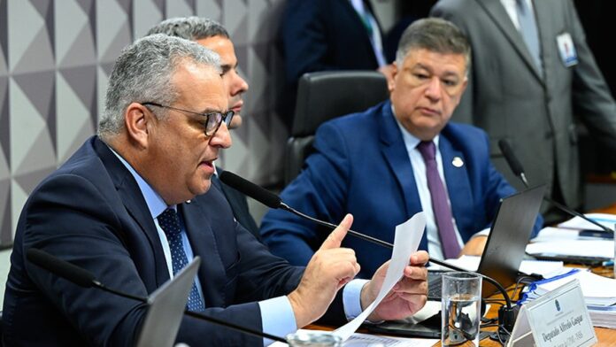 Parlamentares discutem em sessão plenária da CPMI em Brasília com documentos sobre as mesas e telão ao fundo.