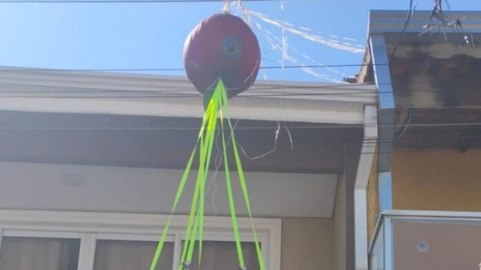 Equipe da Defesa Civil remove balão colorido caído sobre fiação elétrica em rua residencial, sob céu claro.