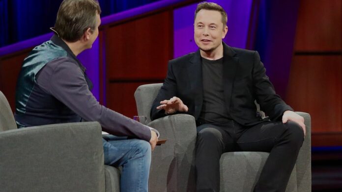 elon-musk-anuncia-f-brica-de-chips-de-us-20-bilh-e Elon Musk em pé diante de um render digital de uma fábrica moderna de semicondutores com logotipo da Tesla ao fundo.