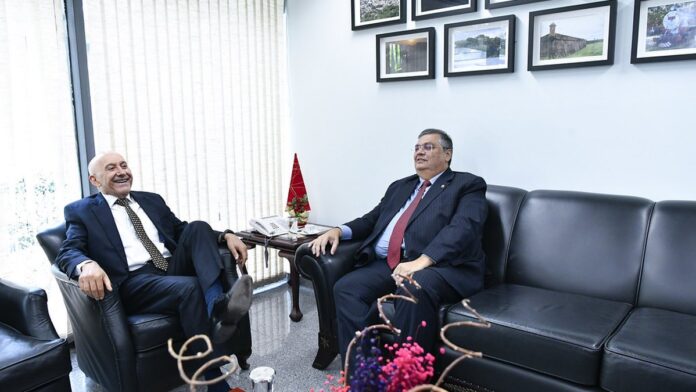 Ministro Flávio Dino em mesa de reunião oficial, ladeado por documentos e microfones, em sessão do STF.