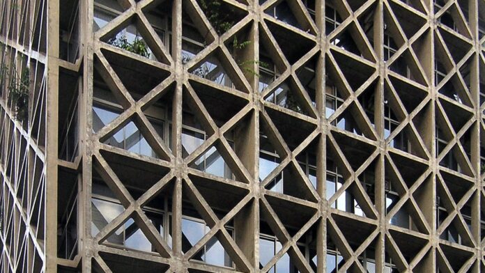 Operário de capacete branco trabalha em obra de grande edifício em construção na cidade de São Paulo.