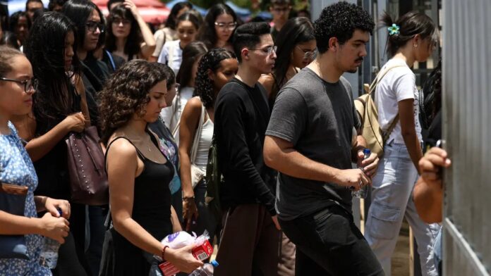 Estudante concentrado preenche folha de gabarito do Enem com lápis em uma sala de aula iluminada.