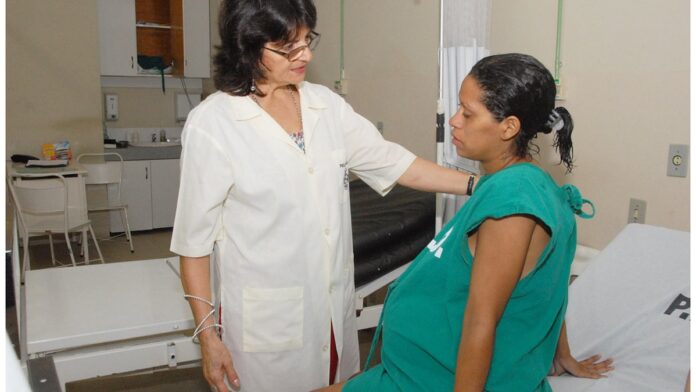 Mulher grávida sentada à mesa de escritório, trabalhando em um computador, com expressão serena.