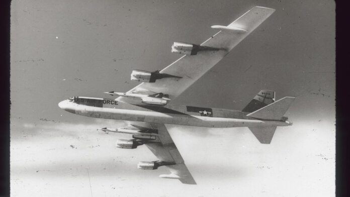 Bombardeiro estratégico B-52 em pleno voo, com silhueta imponente contra um céu nublado.