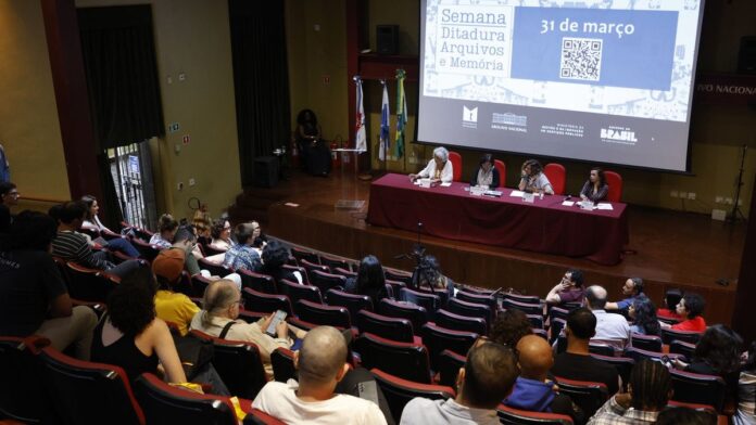 Pessoas observando documentos históricos e fotos em exposição sobre o período da ditadura militar brasileira.