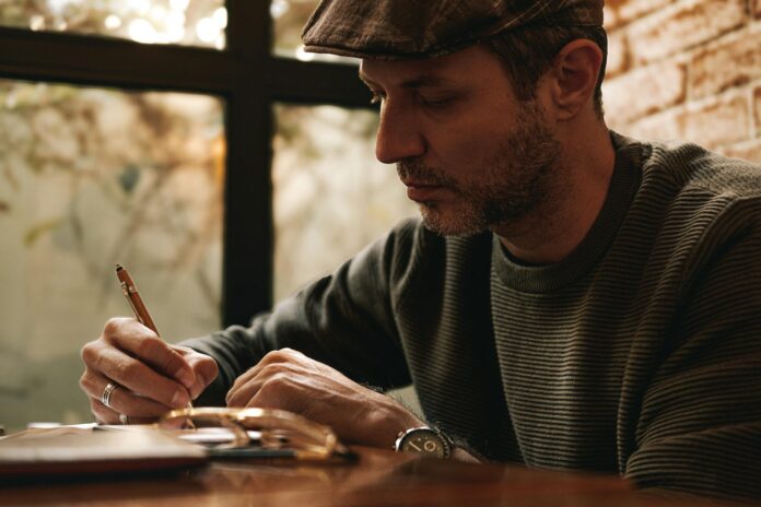 Homem pensativo escrevendo em um caderno com uma caneta em um ambiente interno aconchegante e aconchegante.
