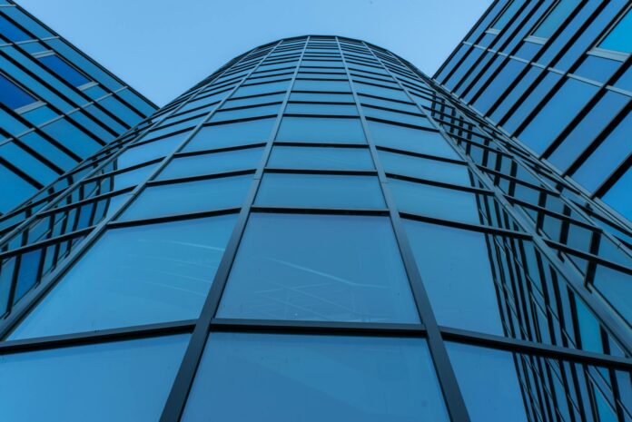 Visão dinâmica da fachada de um arranha-céu contemporâneo com painéis de vidro refletivos.