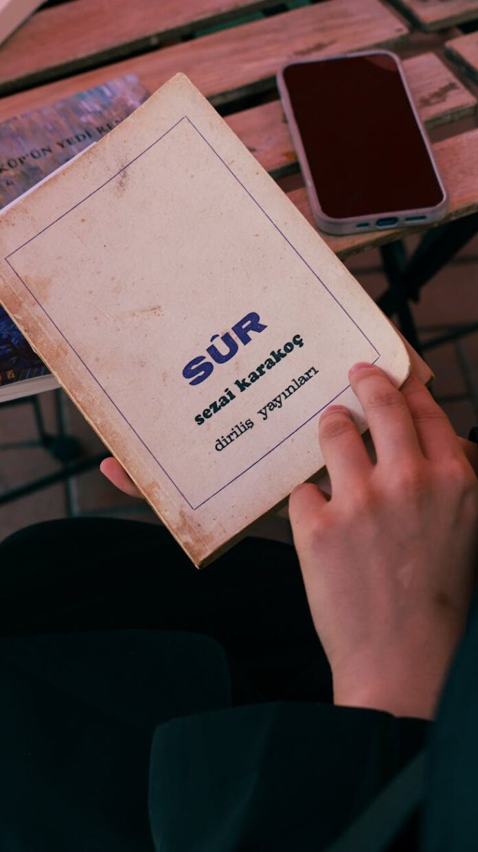 Close de uma pessoa lendo o livro "Sür", de Sezai Karakoç, em um café ao ar livre.