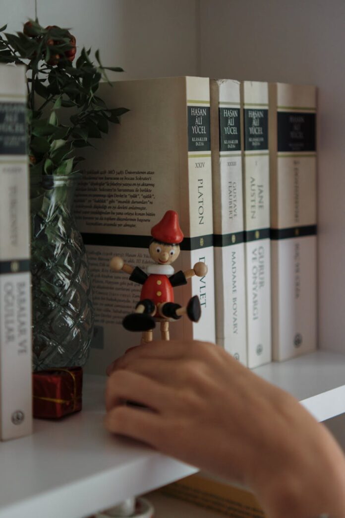 Uma mão alcança uma figura de Pinóquio em uma prateleira com livros e uma planta.
