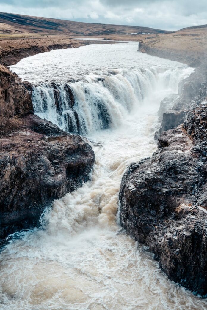 Vista deslumbrante de uma poderosa cachoeira em meio a um terreno rochoso na Islândia.
