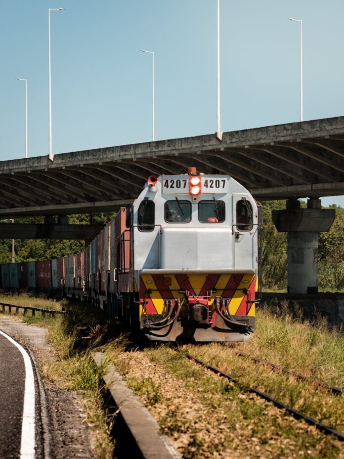 Trem de carga passando sob uma ponte em Laguna, Brasil, durante o dia.