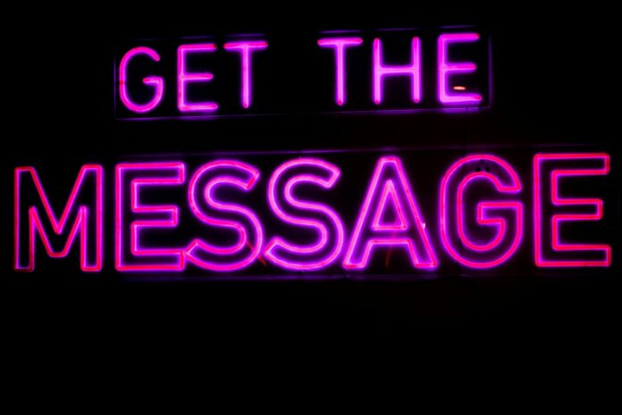 Letreiro de neon rosa vibrante com a frase "Get the Message" (Receba a mensagem) sobre um fundo escuro.