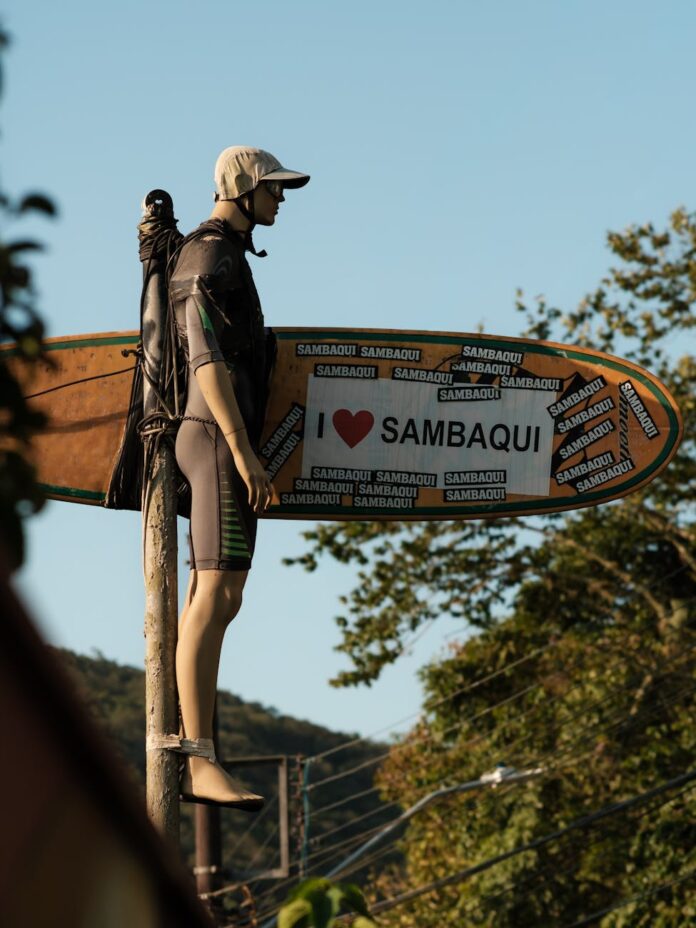 Manequim de surfista com a inscrição 'Eu ❤️ Sambaqui' em um poste, SC, Brasil.