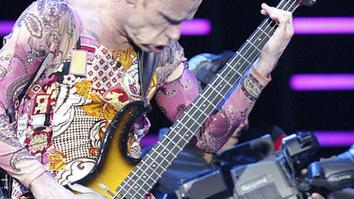 flea-relata-corte-na-cabe-a-ap-s-acidente-inusitad Flea, baixista do RHCP, com um curativo na testa e expressão séria, posa para foto em estúdio de TV.