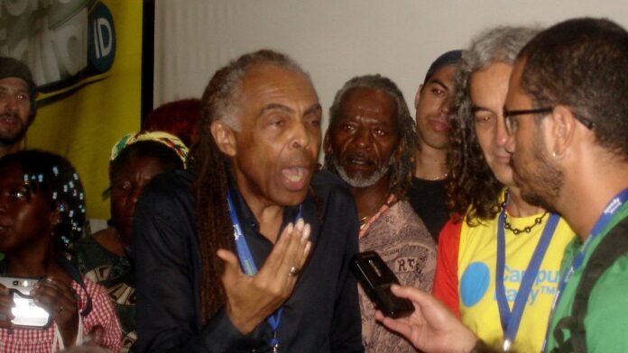 gilberto-gil-finaliza-turn-tempo-rei-com-show-emoc Gilberto Gil canta ao microfone em palco iluminado, durante show de encerramento da turnê Tempo Rei em São Paulo.