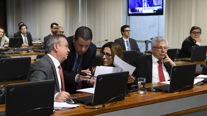 Fachada do prédio do Coaf com placa de identificação e bandeira do Brasil ao fundo sob céu claro.