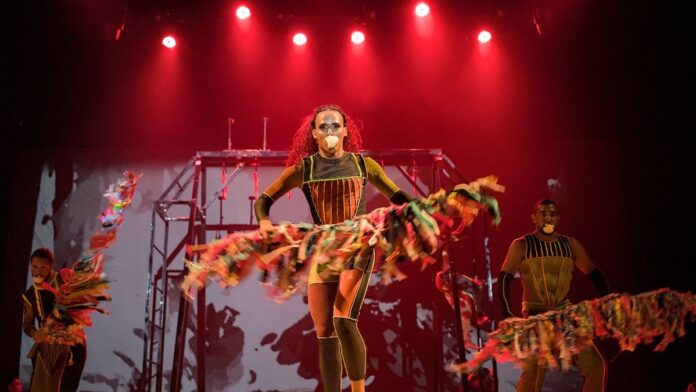 Grupo de pessoas diversas participando de uma oficina de artes em um centro cultural, com telas e pincéis ao fundo.