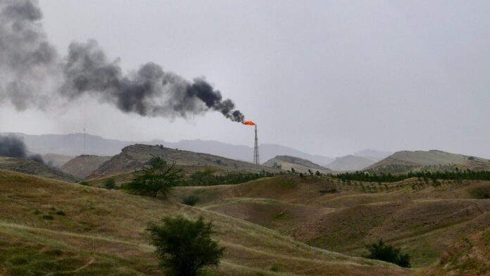 Torres de refinaria de petróleo em meio a um horizonte esfumaçado, sob um céu alaranjado e nublado.