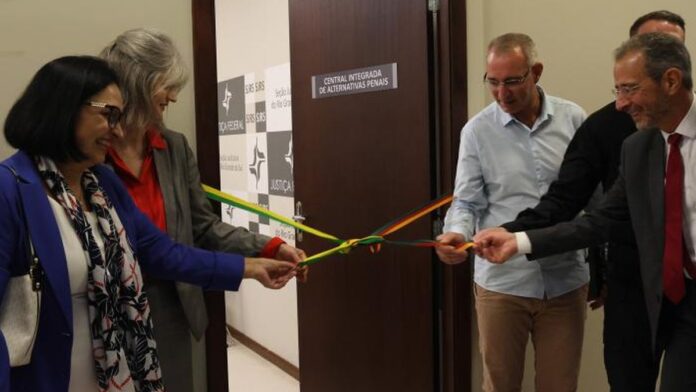 Autoridades posam para foto em frente à placa de inauguração da nova Central de Alternativas Penais em Porto Alegre.