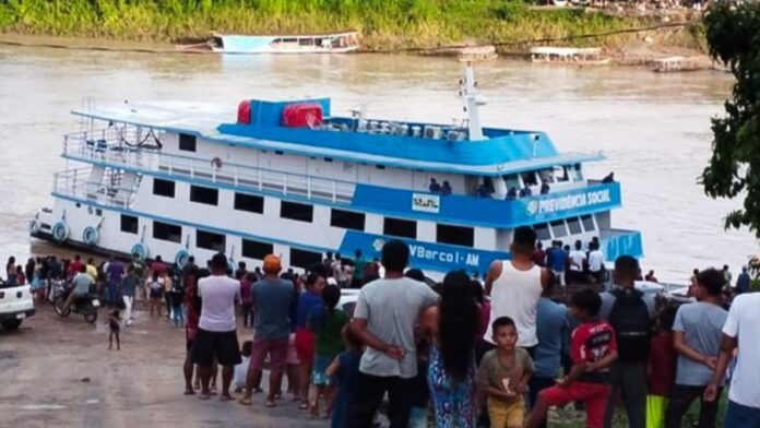Barco do INSS navegando em rio na floresta amazônica para realizar atendimento médico a comunidades ribeirinhas.
