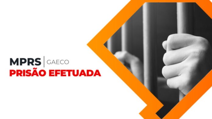 Homem algemado, vestindo camiseta escura, sendo conduzido por policiais civis em frente a uma viatura.