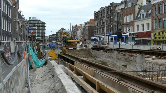 Engenheiro de capacete usa tablet em canteiro de obras, com sobreposição gráfica de estrutura digital em prédio.