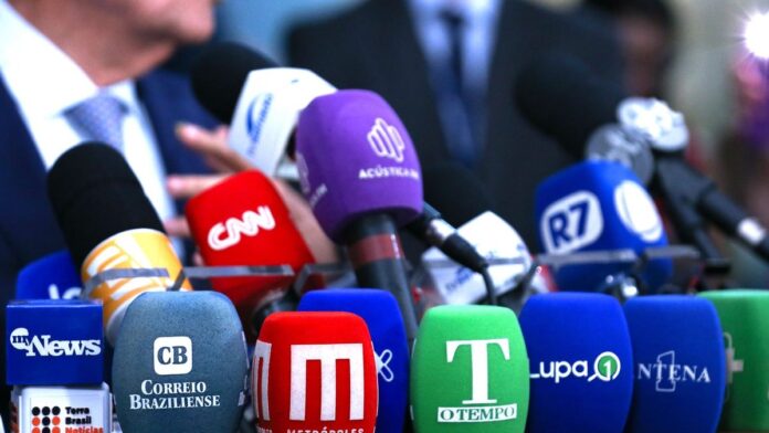 Foto de jornalista posando séria, em plano médio, com expressão de preocupação em ambiente de escritório.