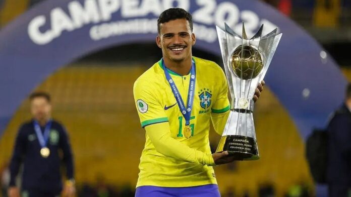 Kaiki veste a camisa da seleção brasileira, sorrindo durante treinamento em campo de futebol.