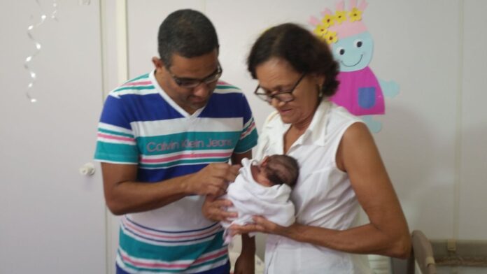 Pai sorridente segura um bebê recém-nascido no colo, transmitindo um momento de afeto e cuidado familiar.