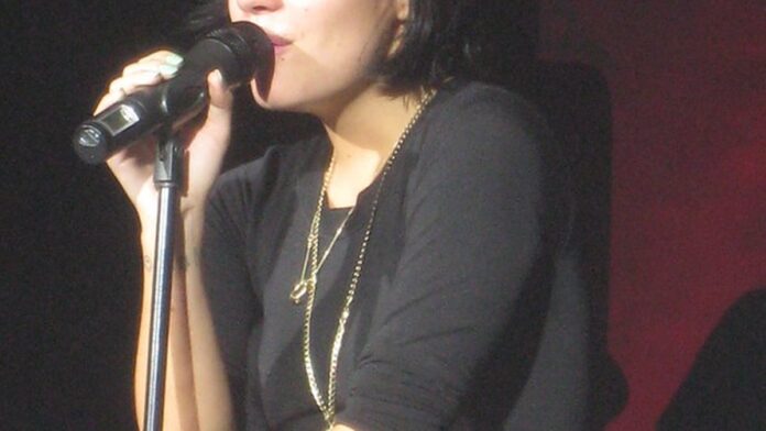 lily-allen-retoma-shows-em-londres-com-foco-no-lbu Lily Allen canta em um palco iluminado de Londres, vestindo figurino moderno durante show focado em seu novo álbum.