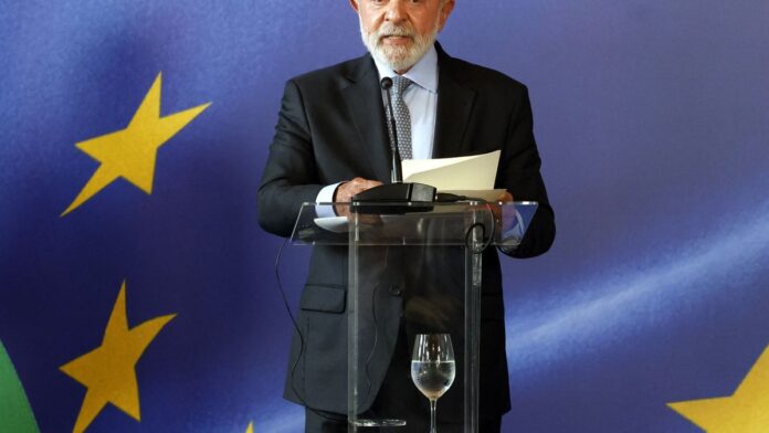 Presidente Lula assina documento oficial em mesa, cercado por autoridades em cerimônia no Palácio do Planalto.