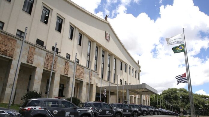 Viaturas da polícia estacionadas em frente a uma residência urbana com policiais conversando na calçada.