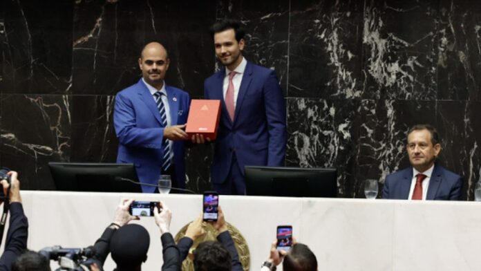 Mateus Simões discursa em cerimônia formal, posicionado em um púlpito com a bandeira de Minas Gerais ao fundo.