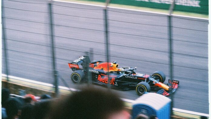 Max Verstappen em traje de piloto, com expressão séria, gesticulando durante coletiva de imprensa no circuito de Suzuka.