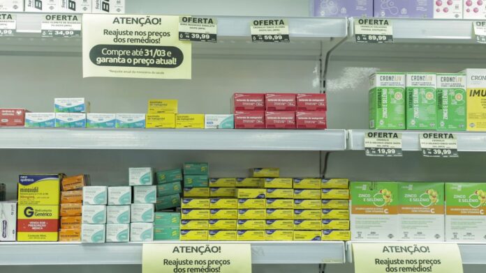 Prateleiras de supermercado com cartazes de farmácia e diversos produtos de saúde expostos ao lado de itens comuns.